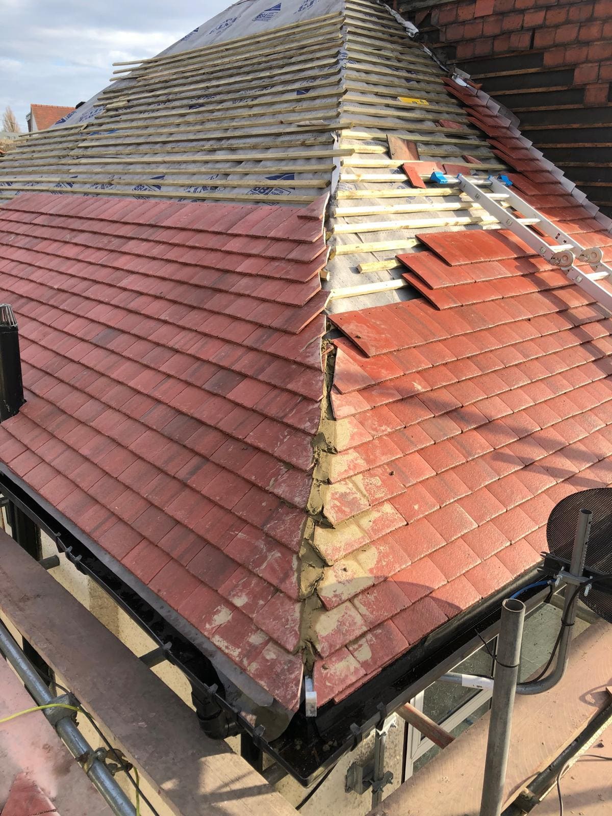 Hip roof re-tile in progress on a London property showing new red clay tiles and mortar bedding