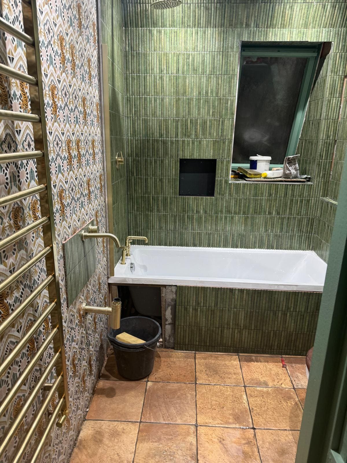 London bathroom refurbishment featuring fluted green tiling, inset niche and brushed brass heated towel rail